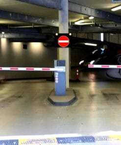 Zablokowana brama wjazdowa do parkingu, oznaczenie zakazu wjazdu. Obiekt oświetlony sztucznym światłem, w tle widoczna kręta droga oraz pojazd wjeżdżający w głąb tunelu. Scena odzwierciedla aspekty bezpieczeństwa pracy i ochrony środowiska w kontekście mobilności i infrastruktury.