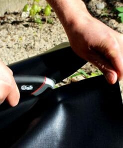 Mężczyzna przytrzymujący czarną folię, używający narzędzia do jej cięcia. Praca z materiałem ma na celu wsparcie działań związanych z ochroną środowiska, stosowana w ekologicznym ogrodnictwie lub zabezpieczeniu wód gruntowych.