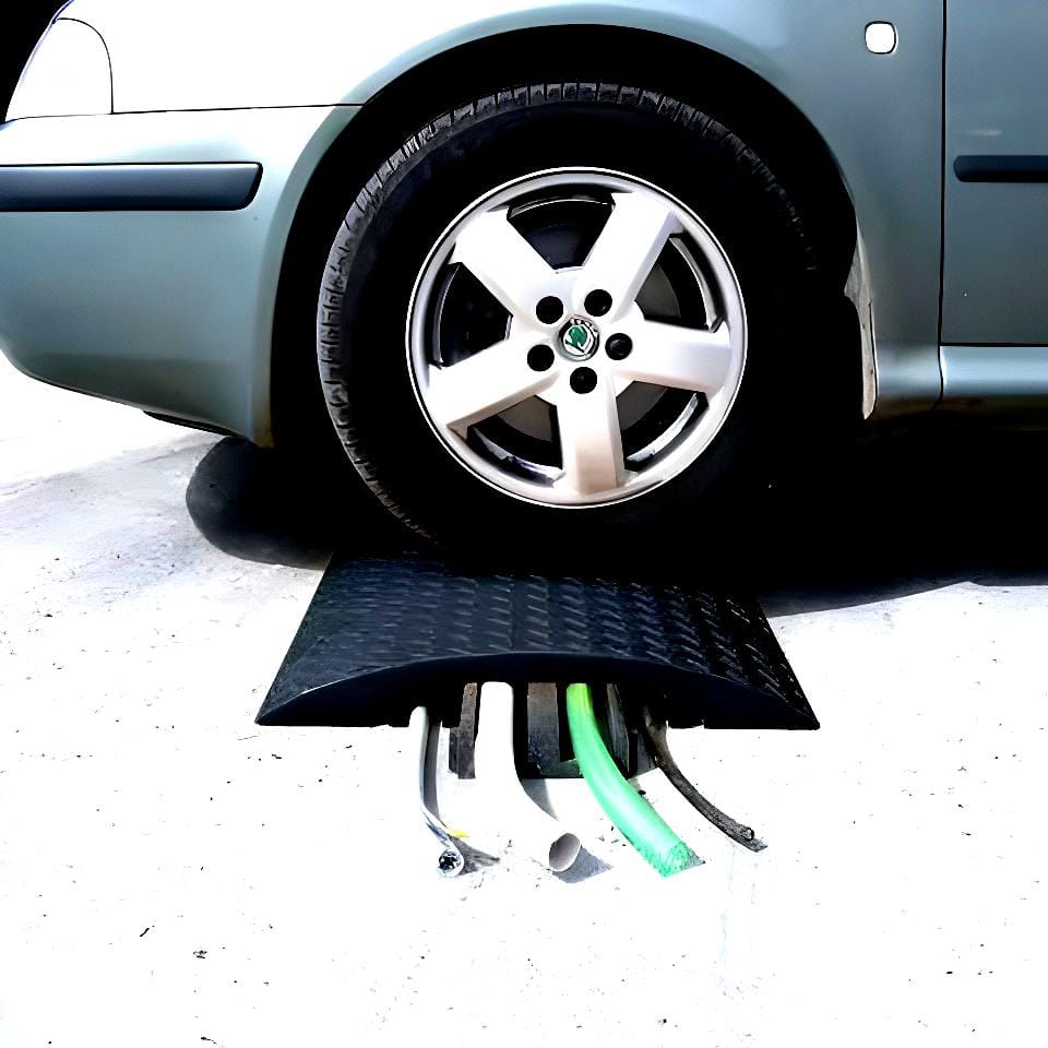 Zbliżenie na koło samochodu stojącego na podjeździe z matą ochronną, pod którą widoczne są węże. Mata zabezpiecza przed uszkodzeniem węży, co wpływa na bezpieczeństwo pracy i ochronę środowiska, redukując ryzyko wycieków i zapewniając odpowiednie środki awaryjne w przypadku awarii.