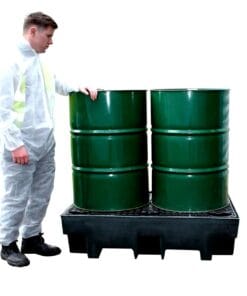 Mężczyzna w kombinezonie ochronnym stoi obok dwóch zielonych bębnów umieszczonych na platformie zabezpieczającej. Scena ilustruje środki awaryjne w kontekście bezpieczeństwa pracy i ochrony środowiska.
