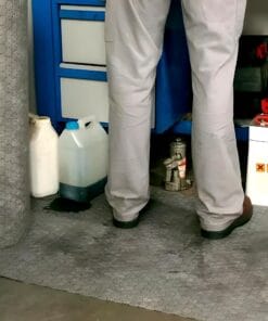 Mężczyzna stojący na podłodze w warsztacie, obok pojemników z płynami chemicznymi oraz narzędziami. W tle widoczna jest niebieska szafka z szufladami. Zdjęcie ilustruje kwestie bezpieczeństwa pracy i zarządzania substancjami niebezpiecznymi w warsztacie, co jest ważne w kontekście ochrony środowiska.