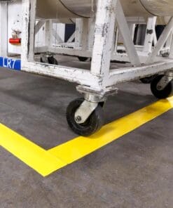 Stabilna platforma na kółkach, z widoczną oznaczoną żółtą linią na podłodze, co wskazuje na potrzebę przestrzegania zasad bezpieczeństwa pracy oraz organizacji przestrzeni roboczej w kontekście ochrony środowiska.