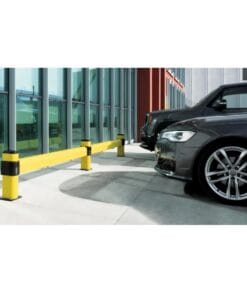 Widok parkingu z żółtą barierką ochronną oddzielającą pojazdy od budynku. Barierka zapobiega uszkodzeniom i zwiększa bezpieczeństwo pracy w strefie parkingowej, co jest istotne w kontekście ochrony środowiska i ekologii.