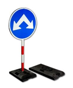 Znaki drogowe: niebieski znak z dwiema białymi strzałkami wskazującymi w prawo i lewo, umieszczony na metalowym słupie z czerwonymi paskami. W zestawie z podstawą zabezpieczającą, zapewniającą stabilność. Użycie w kontekście bezpieczeństwa pracy i ochrony środowiska.