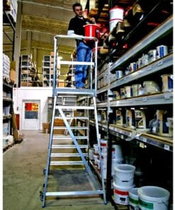 Mężczyzna pracujący na drabinie w magazynie, sięgający po pojemnik z farbą umieszczony na wysokiej półce. Przykład odpowiednich procedur bezpieczeństwa pracy w magazynie.
