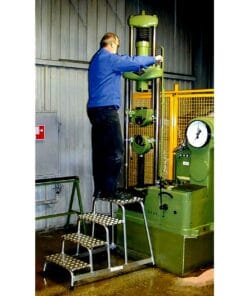 Mężczyzna wykonuje obsługę maszyny przemysłowej na drabinie w zakładzie produkcyjnym. Wykorzystanie odpowiednich środków awaryjnych i bezpieczeństwa pracy jest kluczowe w tej sytuacji, aby zapewnić ochronę środowiska oraz bezpieczne warunki pracy.