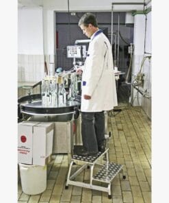 Mężczyzna w białym fartuchu laboratoryjnym pracuje w zakładzie, nadzorując proces obsługi maszyn w laboratorium. Obok niego znajdują się szklane butelki i sprzęt pomiarowy, co wskazuje na zachowanie standardów bezpieczeństwa pracy oraz dbałość o jakość i ekologię w procesie produkcji.