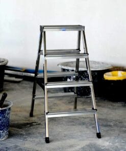 Aluminiowa drabina stojąca na podłodze pomieszczenia budowlanego, w tle widoczne wiadra z farbą, co podkreśla temat bezpieczeństwa pracy oraz ukierunkowanie na odpowiednie środki awaryjne w trakcie remontów.