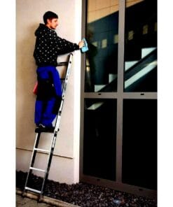 Mężczyzna czyści okno na drabinie przystawnej, dbając o estetykę budynku. Pracuje z niebieską ścierką, stojąc na stabilnej drabinie. Obrona środowiska i dbałość o komfort życia w przestrzeni publicznej.