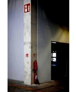 Industrialne wnętrze z oznaczeniami bezpieczeństwa pożarowego, w tym gaśnicą przy ścianie. Wyraźne symbole wskazujące trasę ewakuacyjną oraz miejsce gaśnicy, podkreślające znaczenie środków awaryjnych i bezpieczeństwa pracy w obiektach.