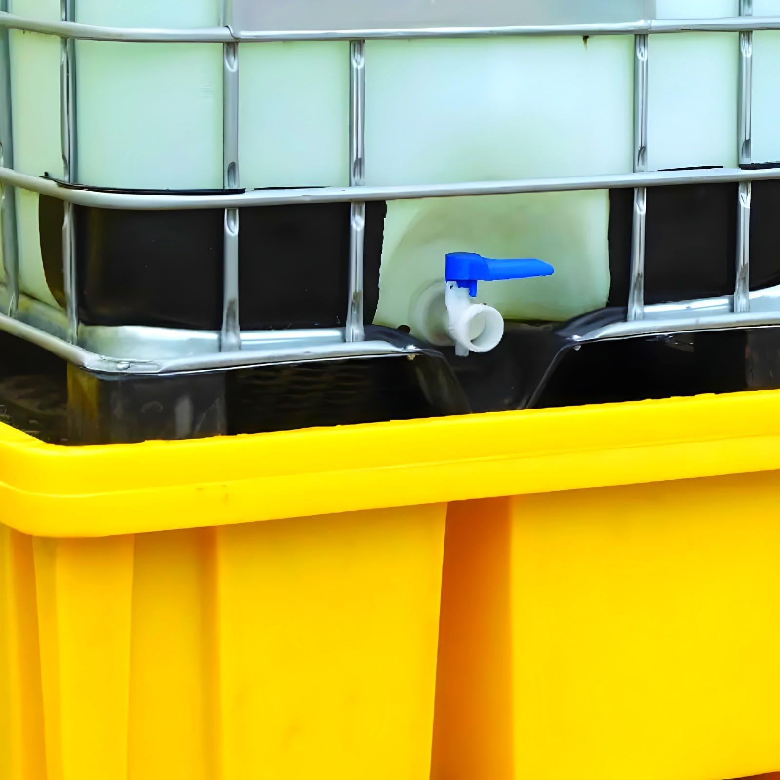 Zbiornik z płynem chemicznym umieszczony na żółtej podstawie, z zaworem odpływowym w niebieskim kolorze, służący do przechowywania substancji wymagających monitorowania w kontekście bezpieczeństwa pracy i ochrony środowiska.